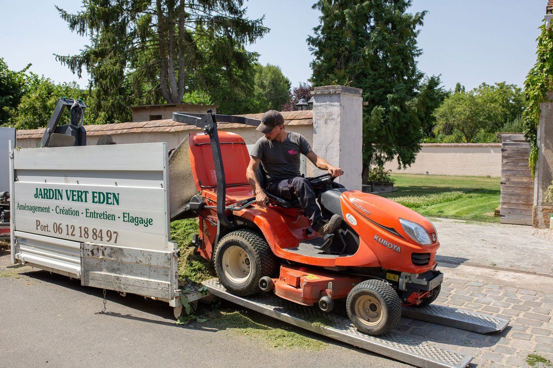 Professionnel de Jardin Vert Eden déchargeant le réservoir d'herbe coupée d'un véhicule de tonte dans une remorque