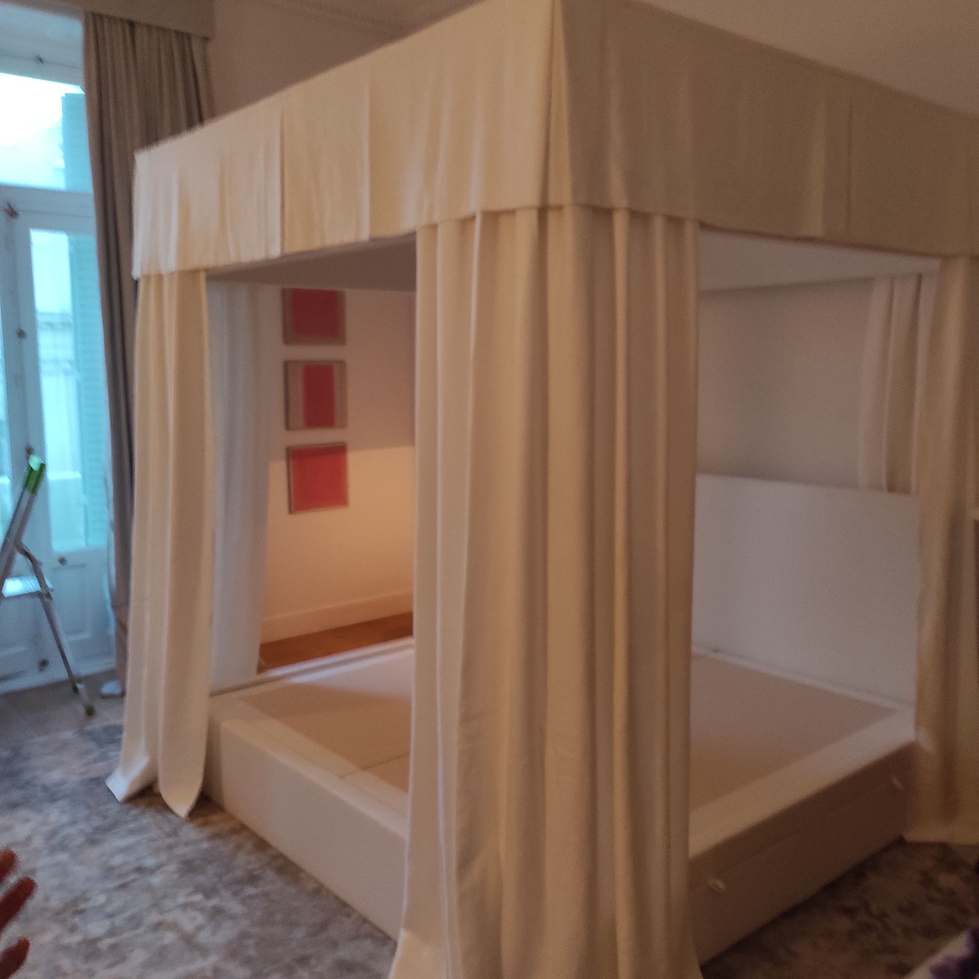 Cama con dosel con cortinas de tela color crema en una habitación.