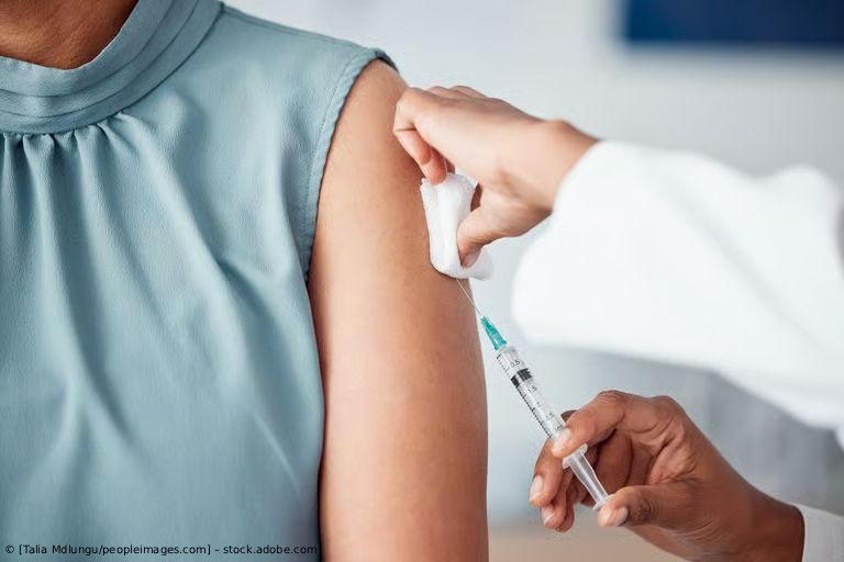 Eine medizinische Fachkraft verabreicht einer Patientin in einem blauen ärmellosen Oberteil eine Schulterinjektion.