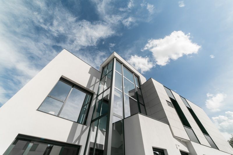 Edificio blanco moderno con grandes ventanales contra un cielo azul parcialmente nublado.
