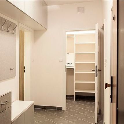 Pasillo con paredes blancas, armario y puerta abierta. Suelo de baldosas grises y perchero.