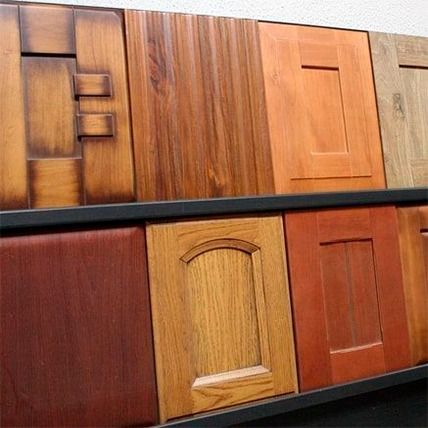 Muestras de puertas de gabinetes de madera en varios estilos y acabados exhibidas en un estante.