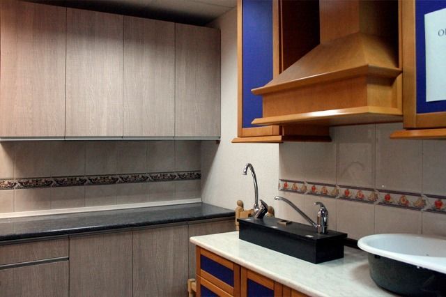 Cocina con gabinetes de madera clara, encimera oscura, campana extractora y protector contra salpicaduras de azulejos con borde decorativo.