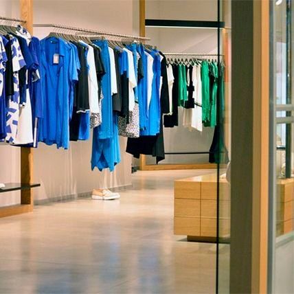 Interior de tienda de ropa con estantes de vestidos coloridos y otras prendas.