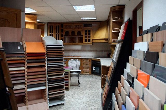 Sala de exposición de gabinetes de cocina con muestras de madera y azulejos, vitrinas y una cocina de prueba.