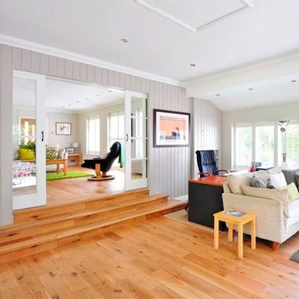 Sala de estar con piso de madera y puerta abierta a otra habitación, paredes color canela, sofá color crema y una silla negra.