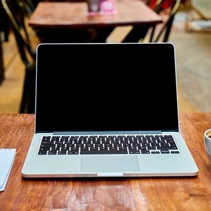 Computadora portátil con pantalla negra sobre una mesa de madera, entorno de cafetería.