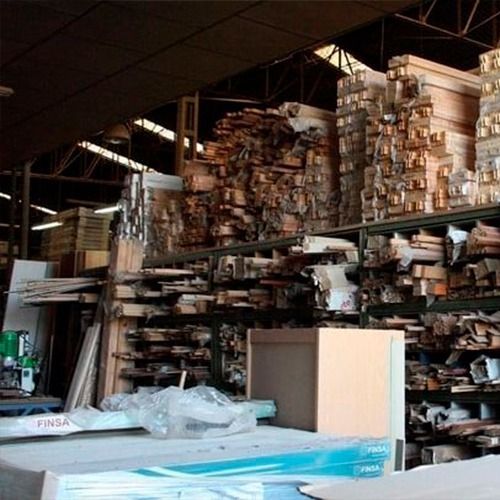 Interior de almacén lleno de pilas de madera y troncos en estantes.