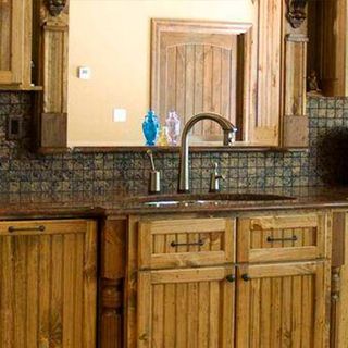 Cocina rústica con gabinetes de madera, grifo de cobre, protector contra salpicaduras marrón y fregadero.