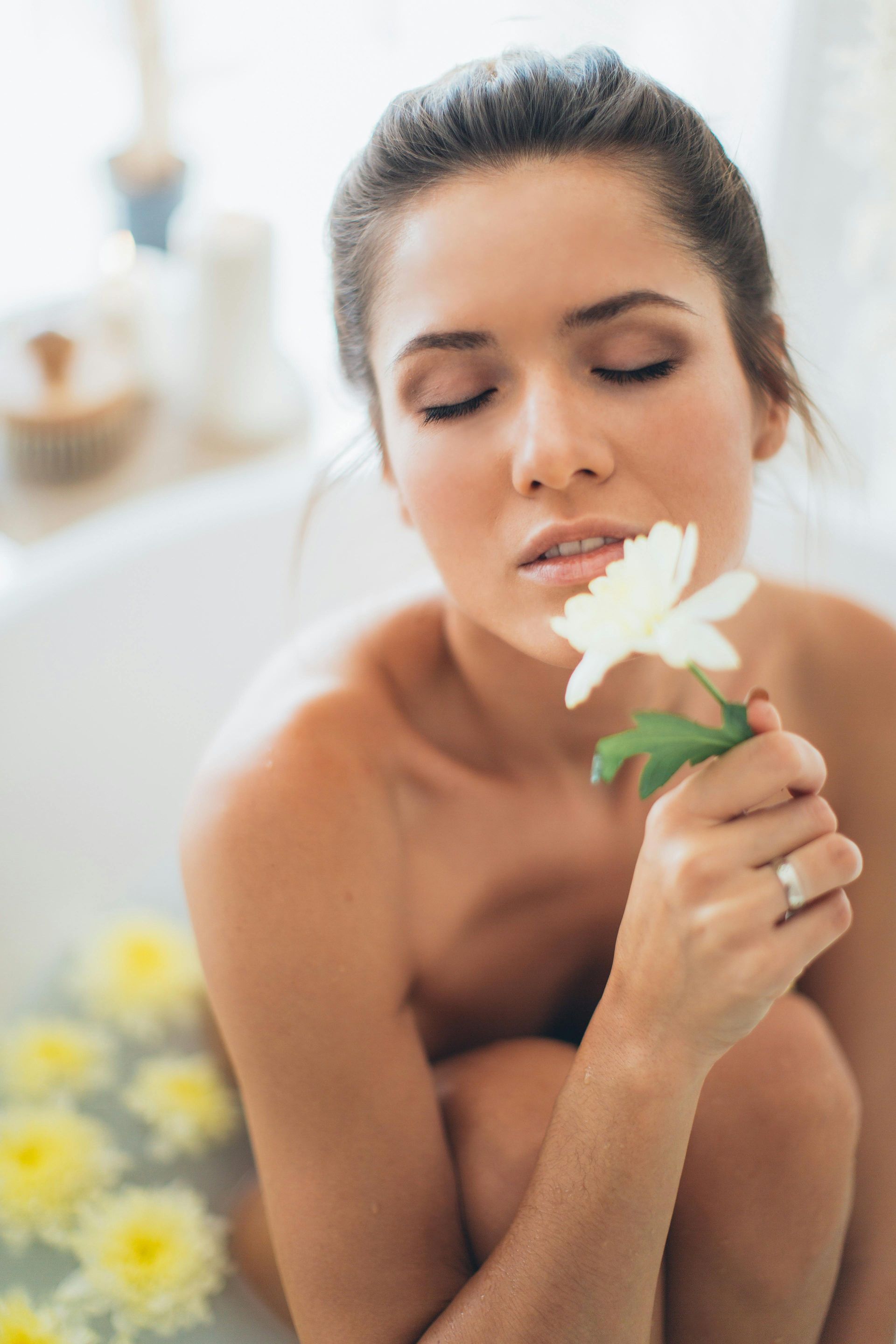 Mujer en la bañera, sosteniendo una flor blanca, ojos cerrados, rodeada de flores amarillas.