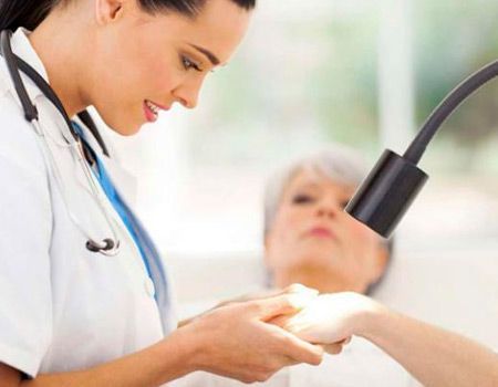 Una médica examina la mano de un paciente bajo una luz.