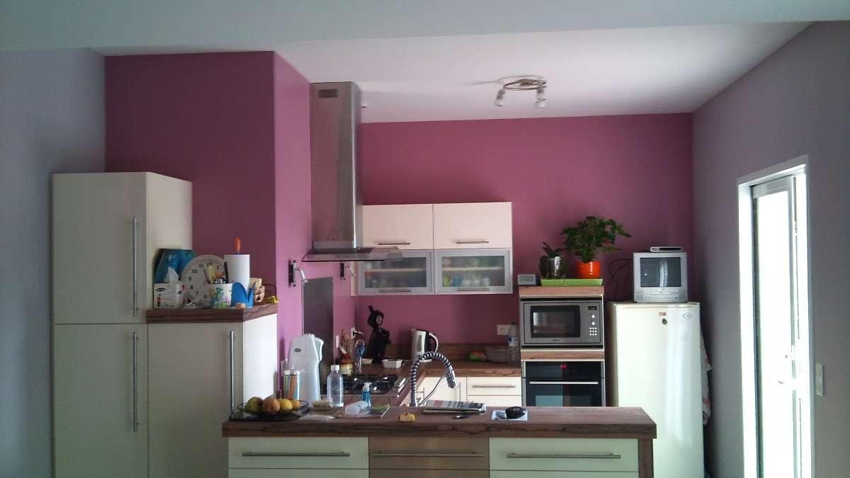 Petite cuisine aux murs violets, placards blancs, un plan de travail et une fenêtre sur la droite