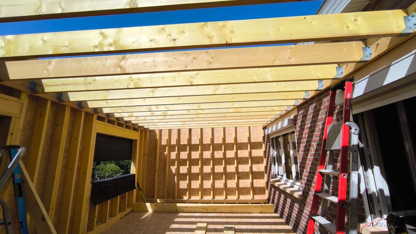Intérieur d'une structure en bois en construction, avec des poutres apparentes et une échelle appuyée contre le mur.