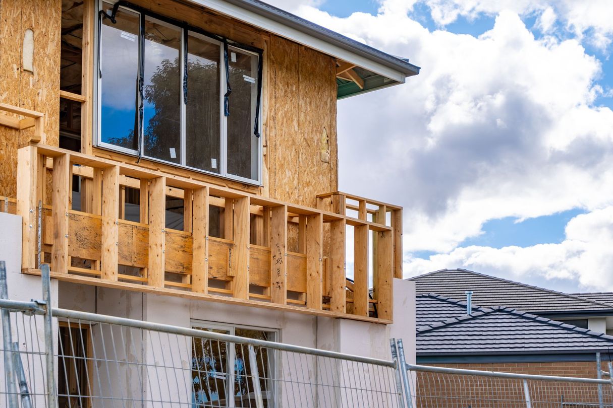 Maison partiellement construite avec un revêtement en contreplaqué et un balcon inachevé.