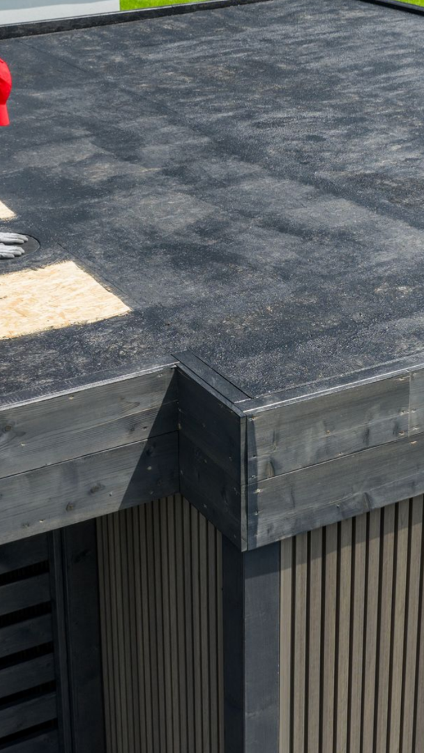 Toiture avec une membrane plate gris foncé et une bordure métallique au-dessus.