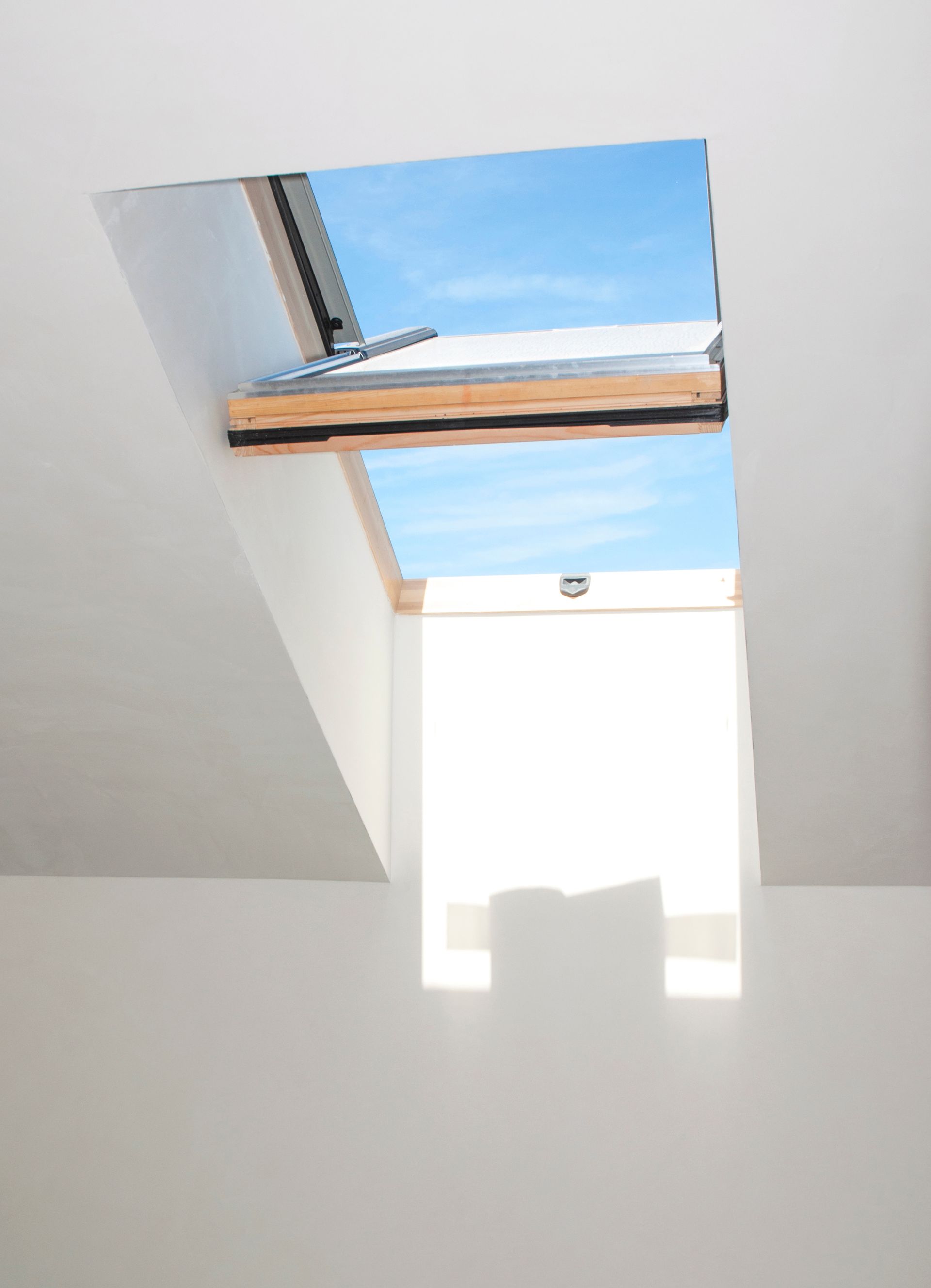 Fenêtre de toit ouverte dans un plafond blanc, laissant apparaître le ciel bleu.