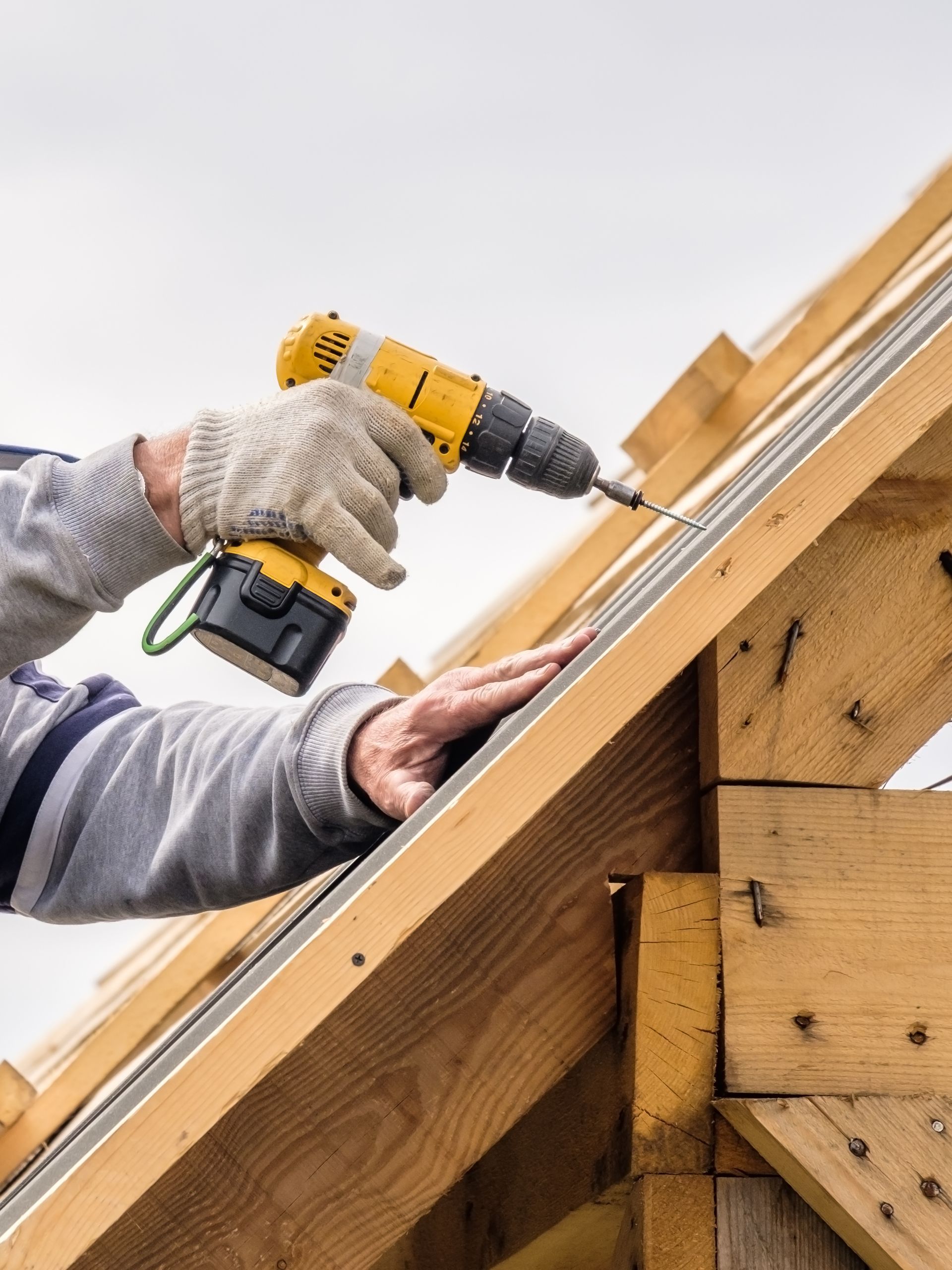 Ouvrier utilisant une perceuse pour installer des vis sur une charpente de toit en bois.