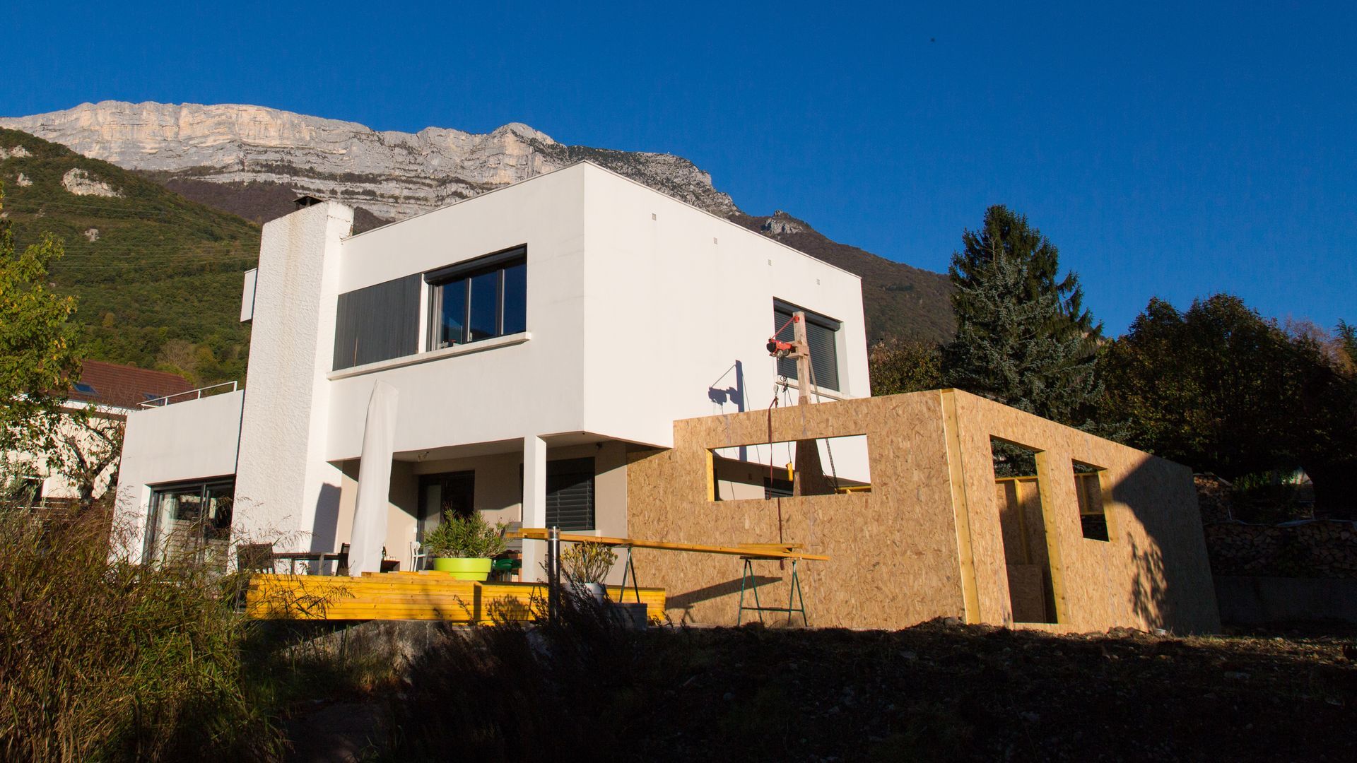 Maison blanche moderne avec une extension en bois à flanc de colline.