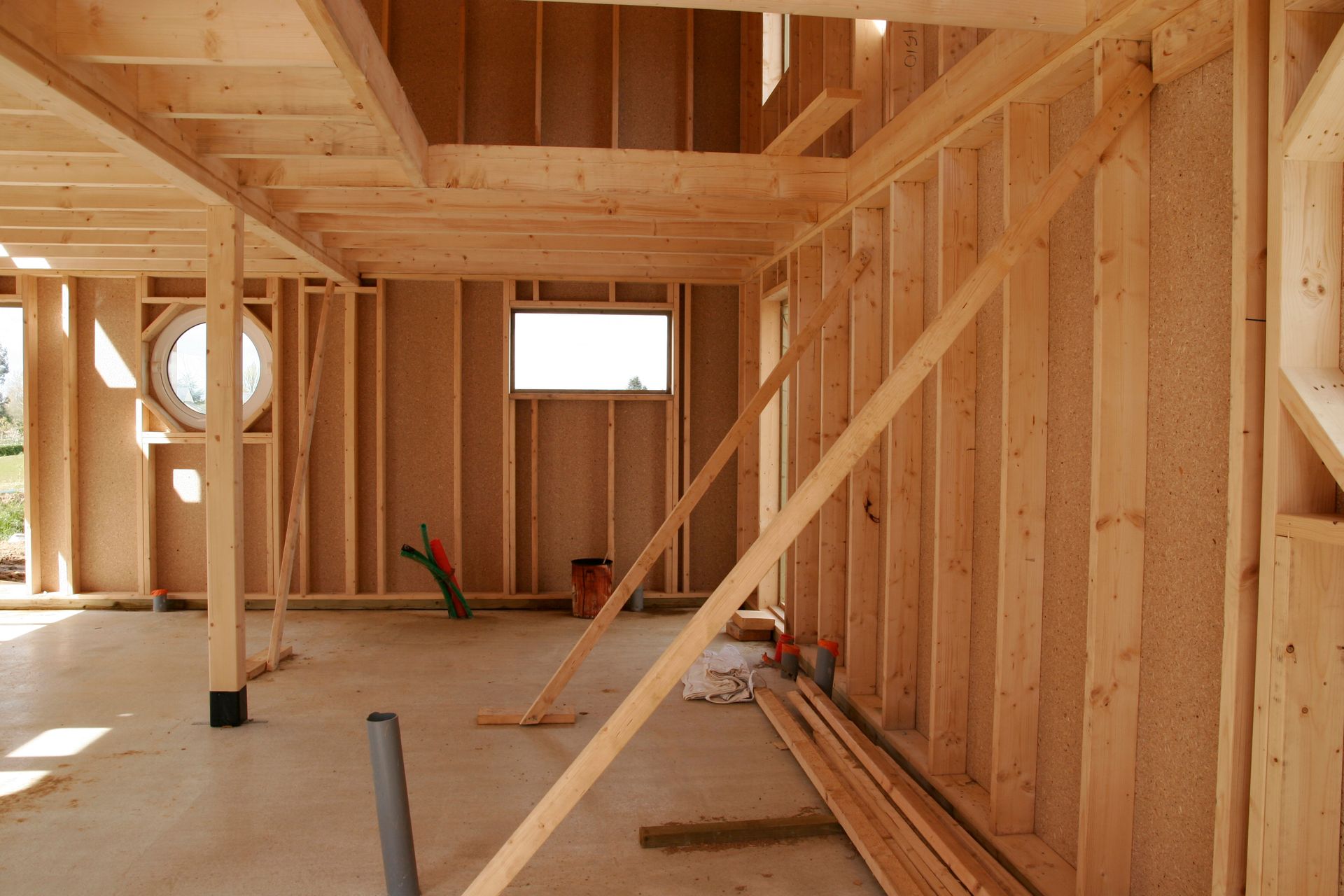 Intérieur d'une maison à ossature bois en construction, avec montants, poutres et ouverture de fenêtre apparents.