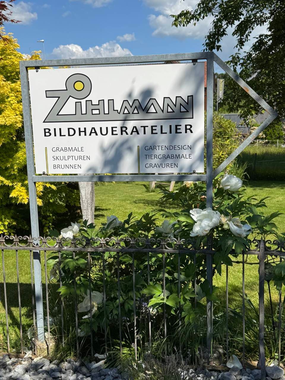 Schild für „BILDHAUEREI“ in einer grasbewachsenen Freiluftanlage hinter einem schwarzen Zaun.