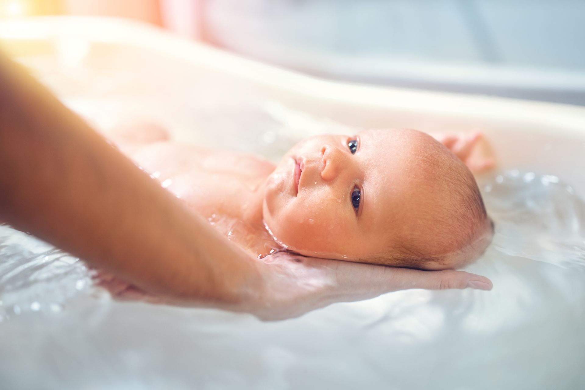 Bébé allongé dans une main pendant un bain doux, avec de l'eau tiède et une lumière chaude