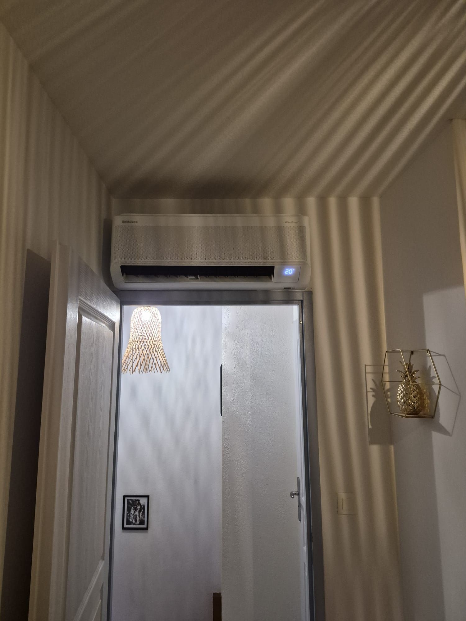 Couloir étroit aux murs rayés, une porte blanche, des appliques murales et un climatiseur au-dessus de la porte.