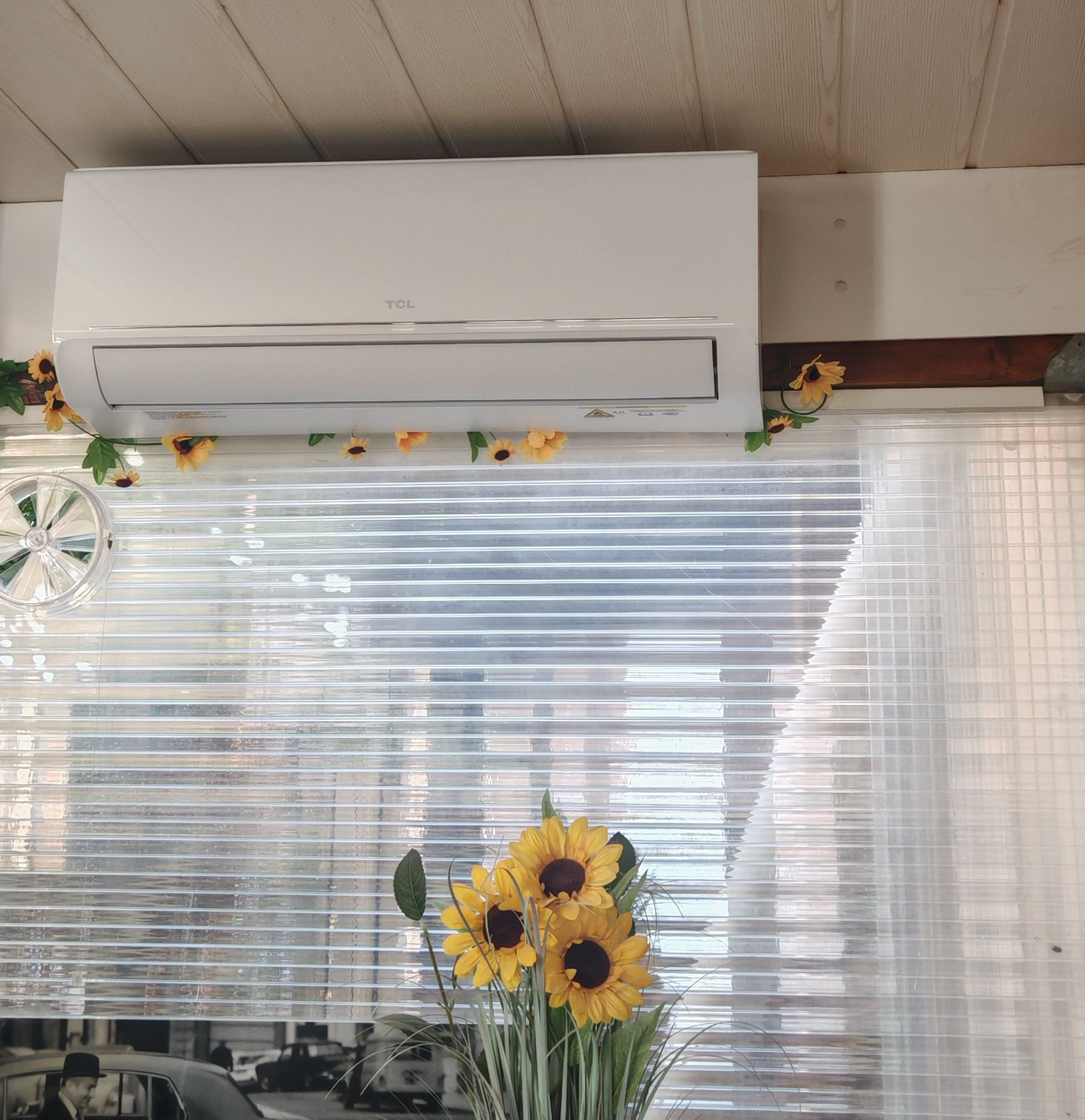 Climatiseur mural blanc au-dessus d'une fenêtre avec des stores voilages et un décor de tournesols