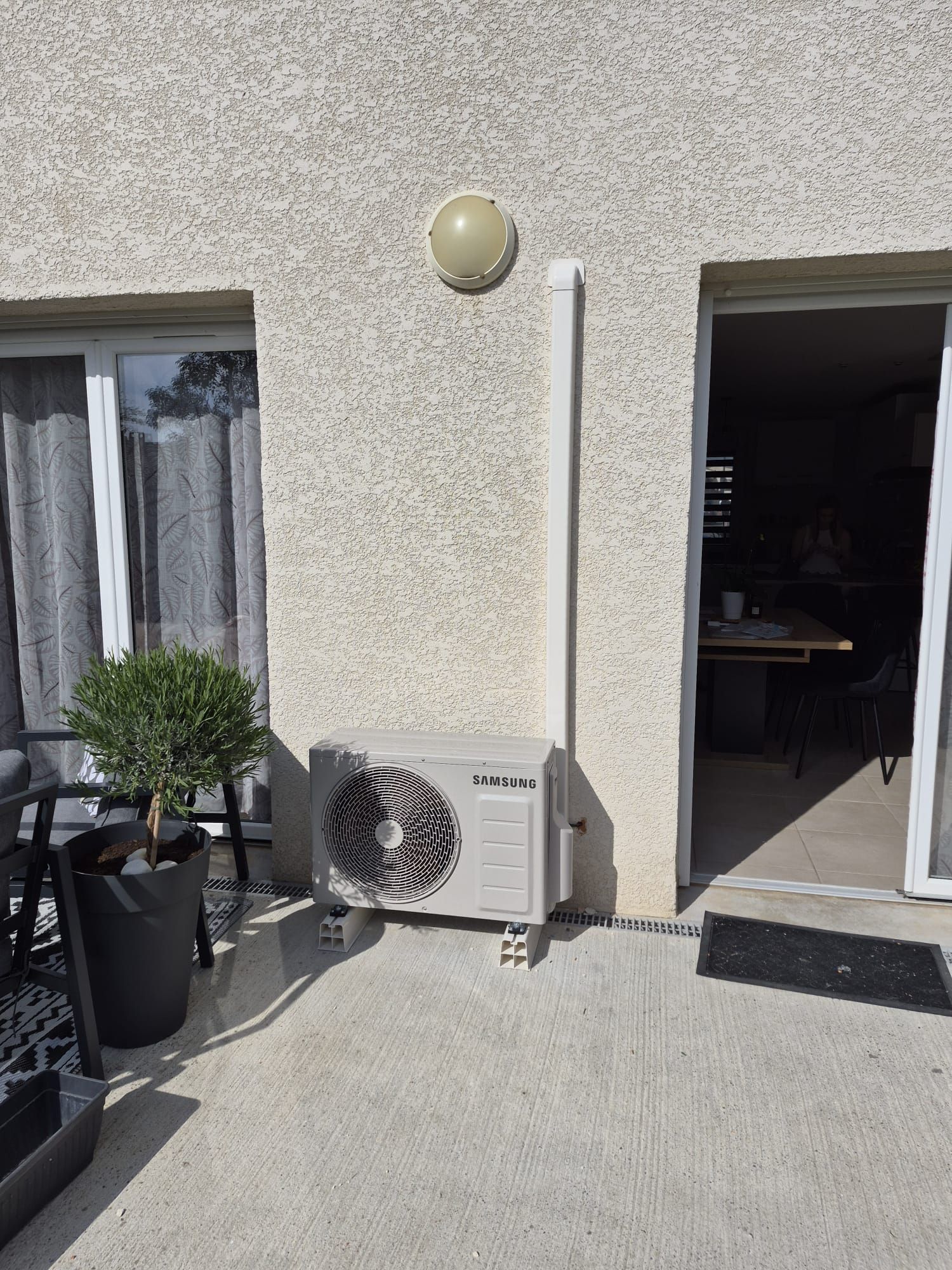 Patio avec climatiseur, plantes en pot et porte ouverte à côté d'un mur en stuc.
