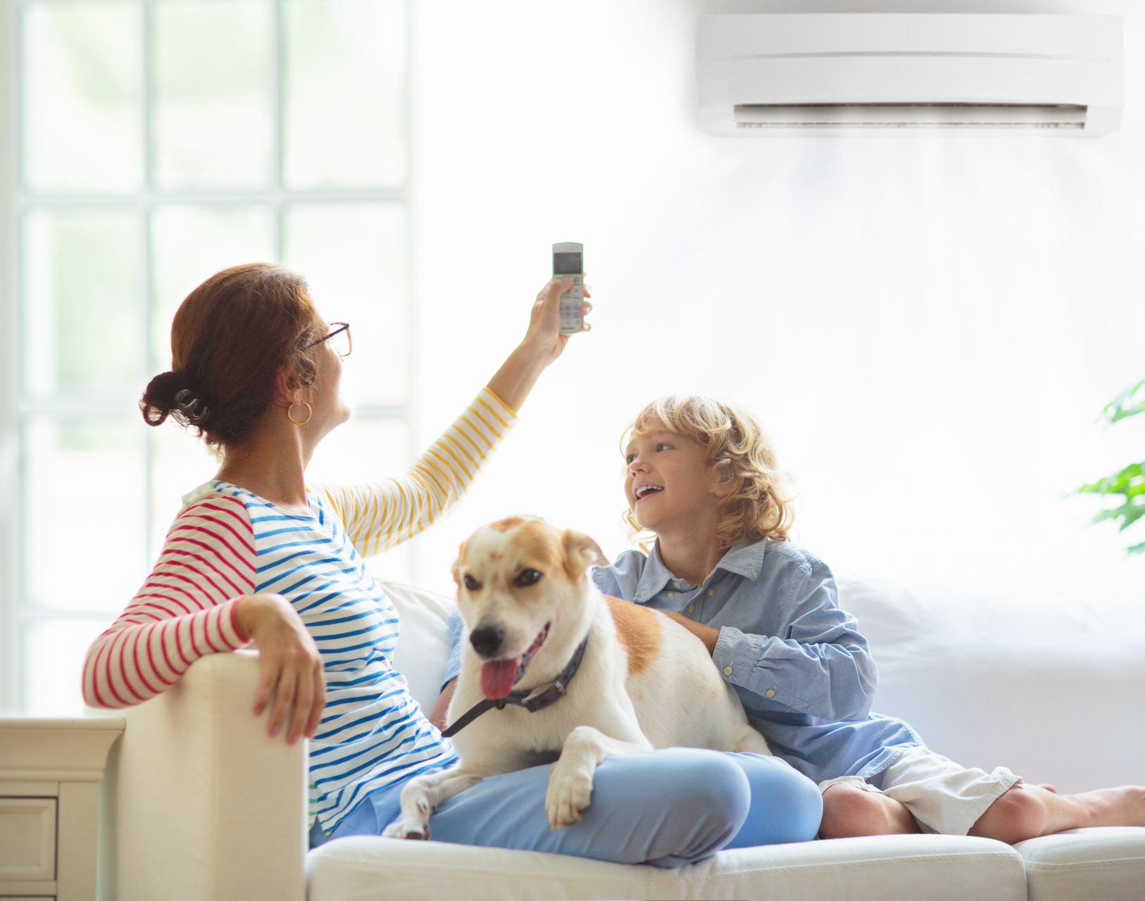 Une mère de famille avec son enfant et son chien régle sa clim avec une télécommande.