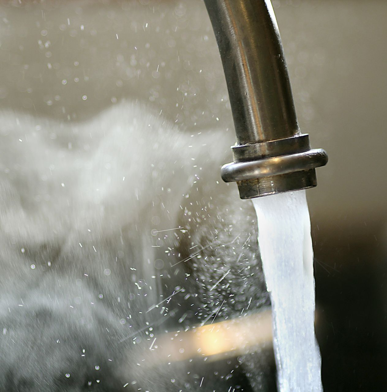 Eau chaude qui coule d'un robinet en acier inoxydable et qui éclabousse l'évier.