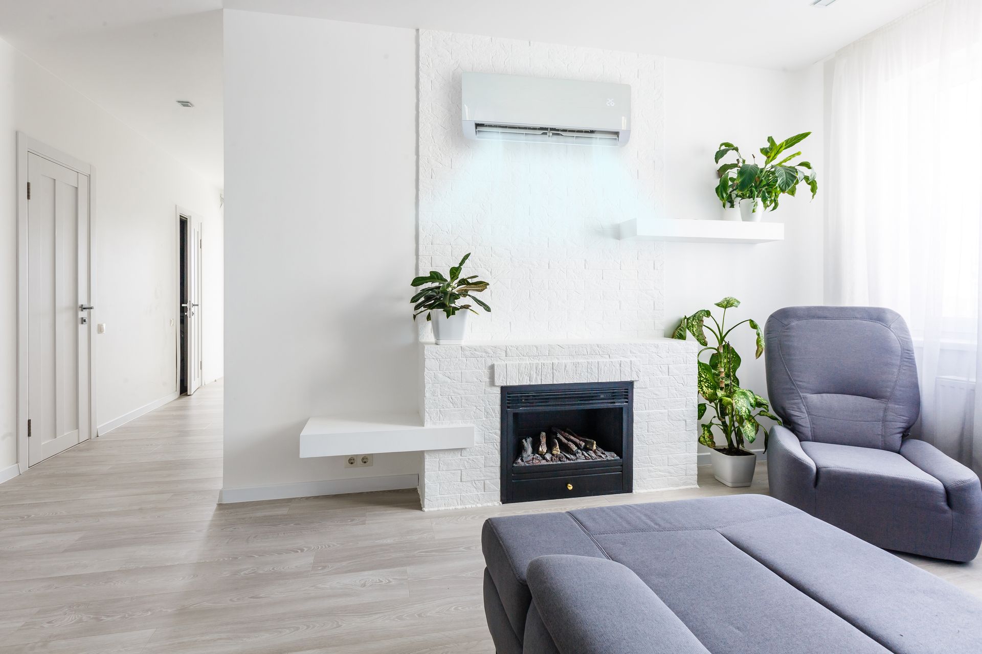 Salon moderne et lumineux avec cheminée blanche, fauteuils gris et plantes en pot