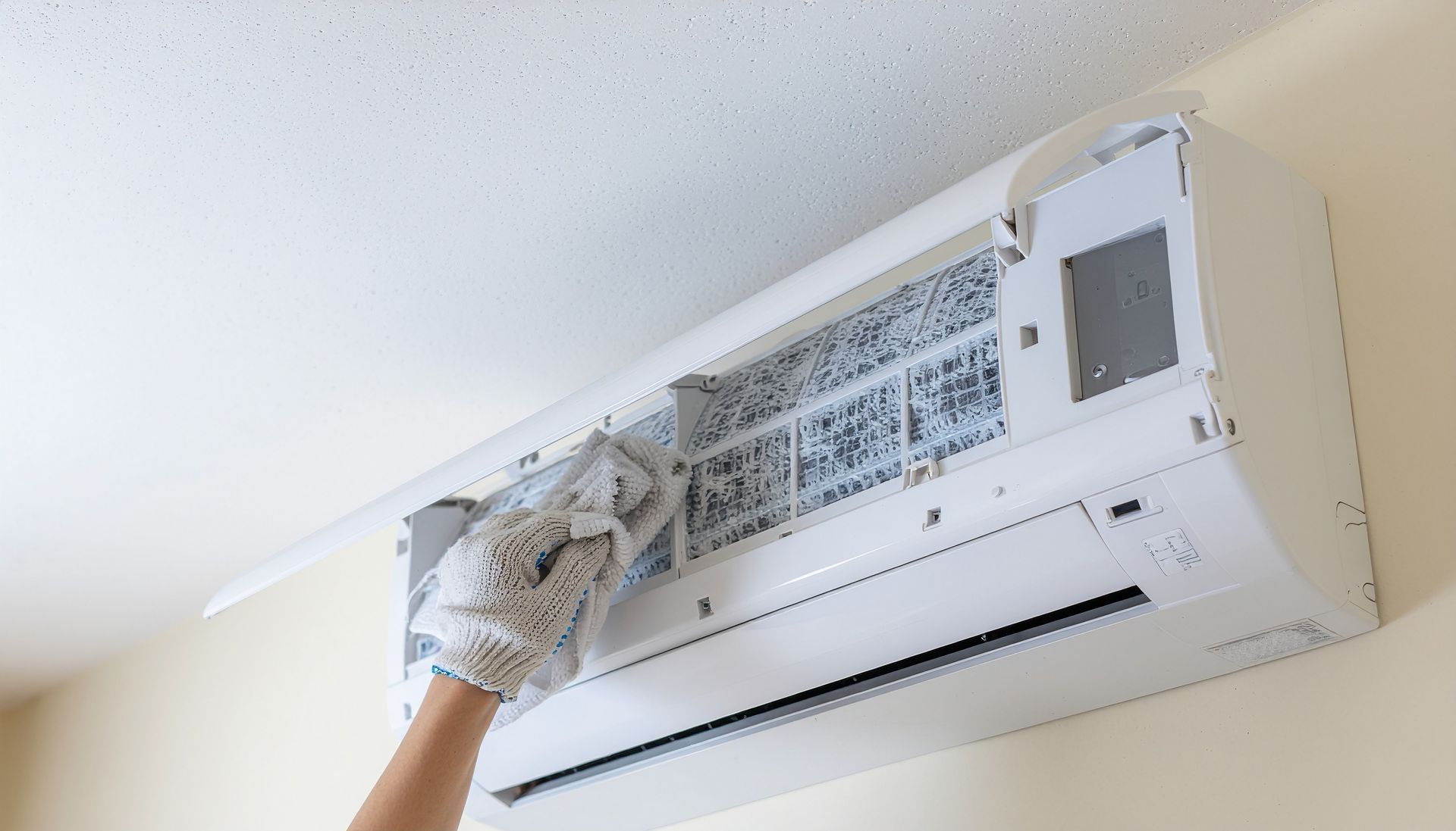 Main gantée nettoyant un filtre de climatiseur sur un appareil mural