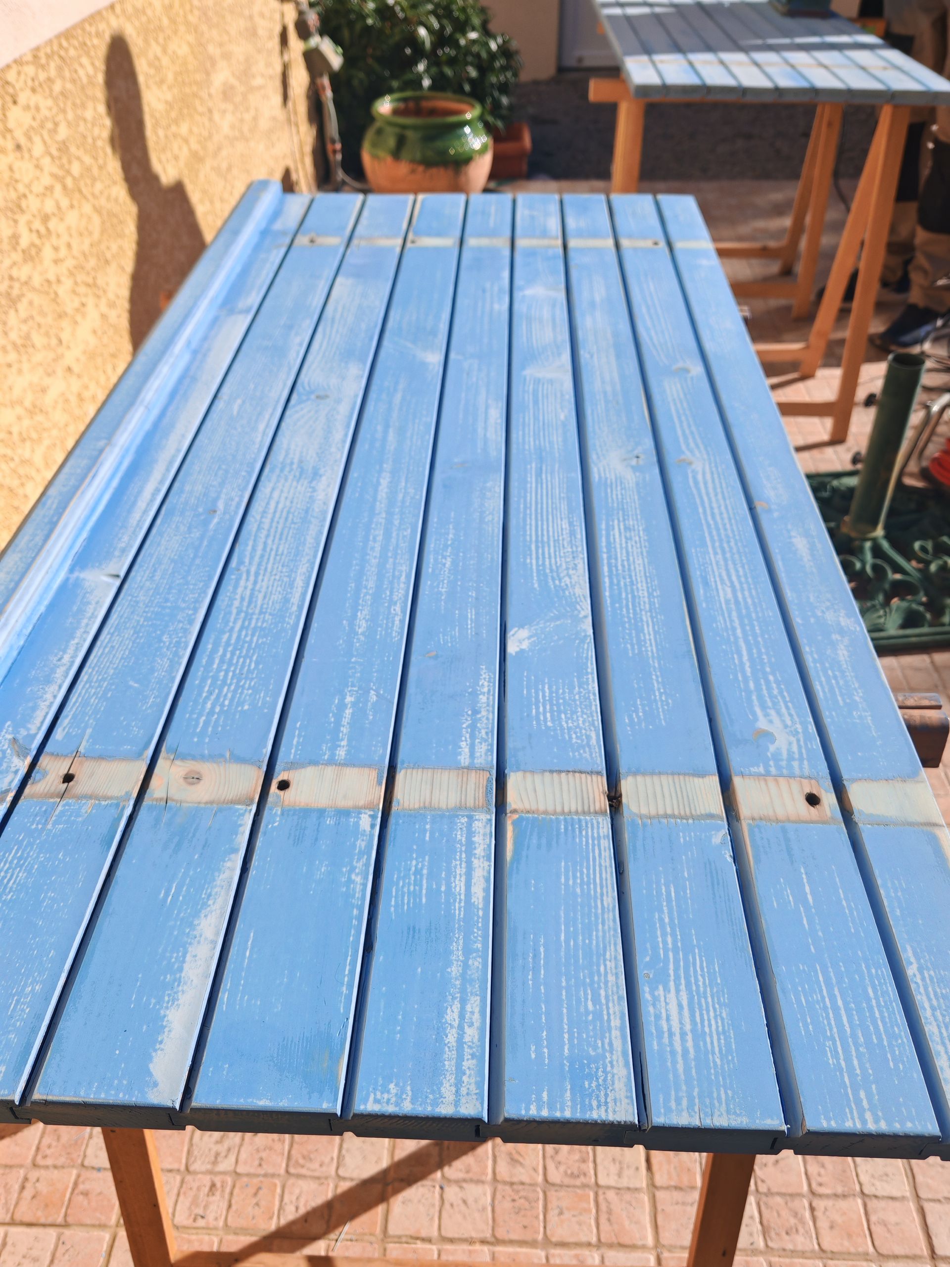 Volet en bois peint en bleu sur une terrasse ensoleillée, vue de dessus.