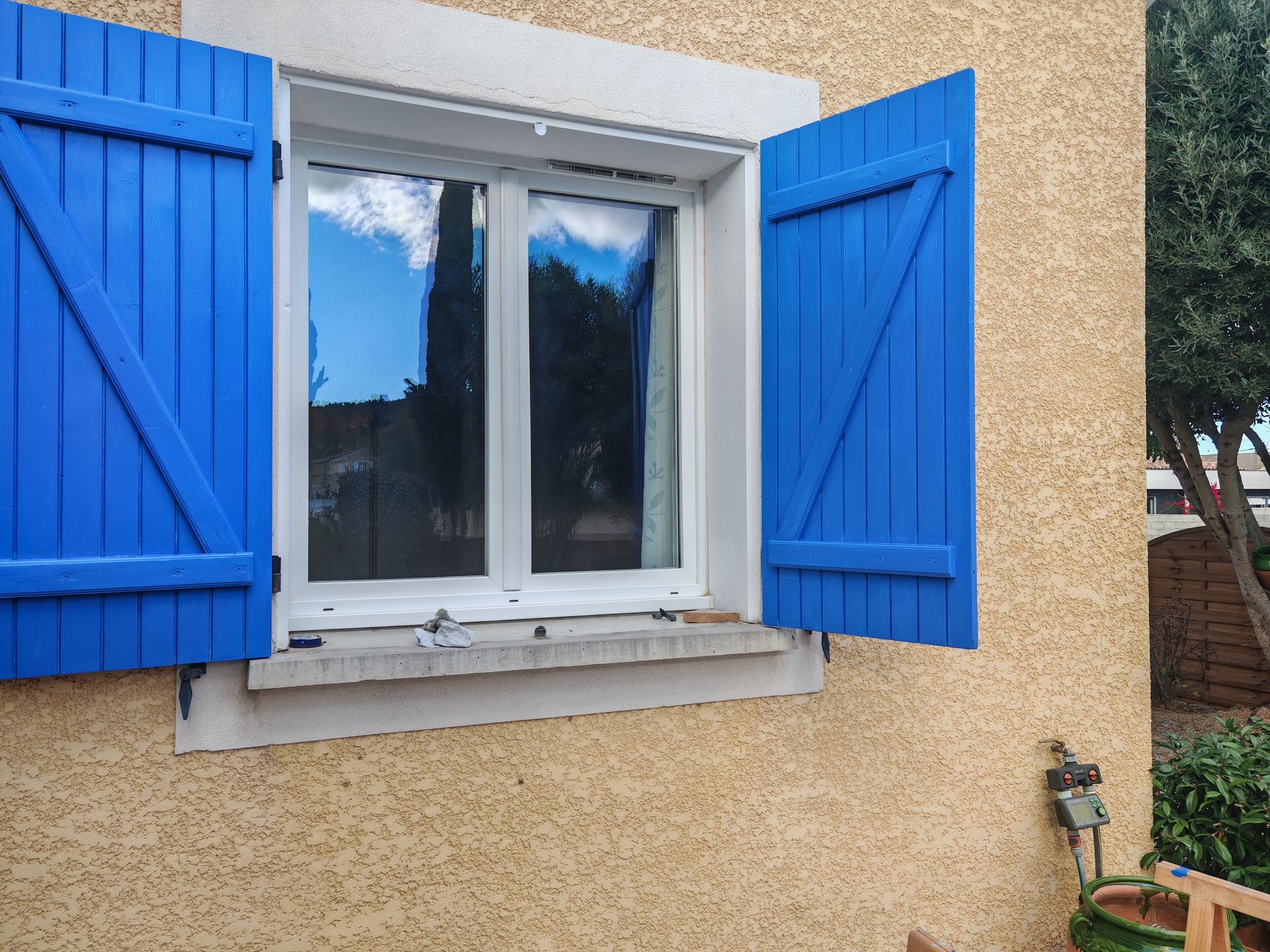 Fenêtre avec des volets bleus ouverts et mur en stuc beige