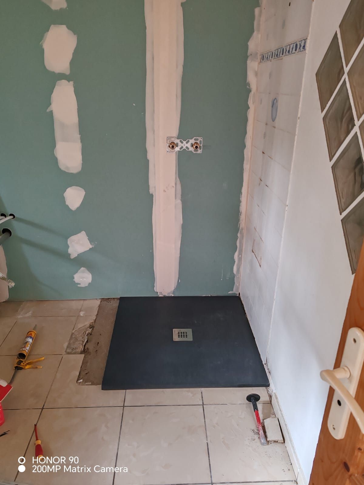 Salle de bains partiellement rénovée avec sol carrelé, murs verts et receveur de douche foncé posé au sol.