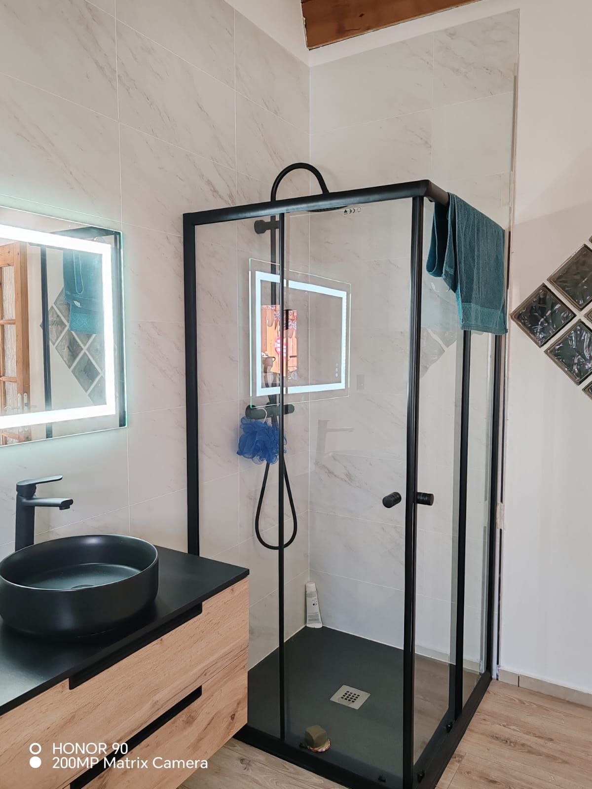 Salle de bains moderne avec cabine de douche en verre, lavabo noir, miroir mural et murs carrelés