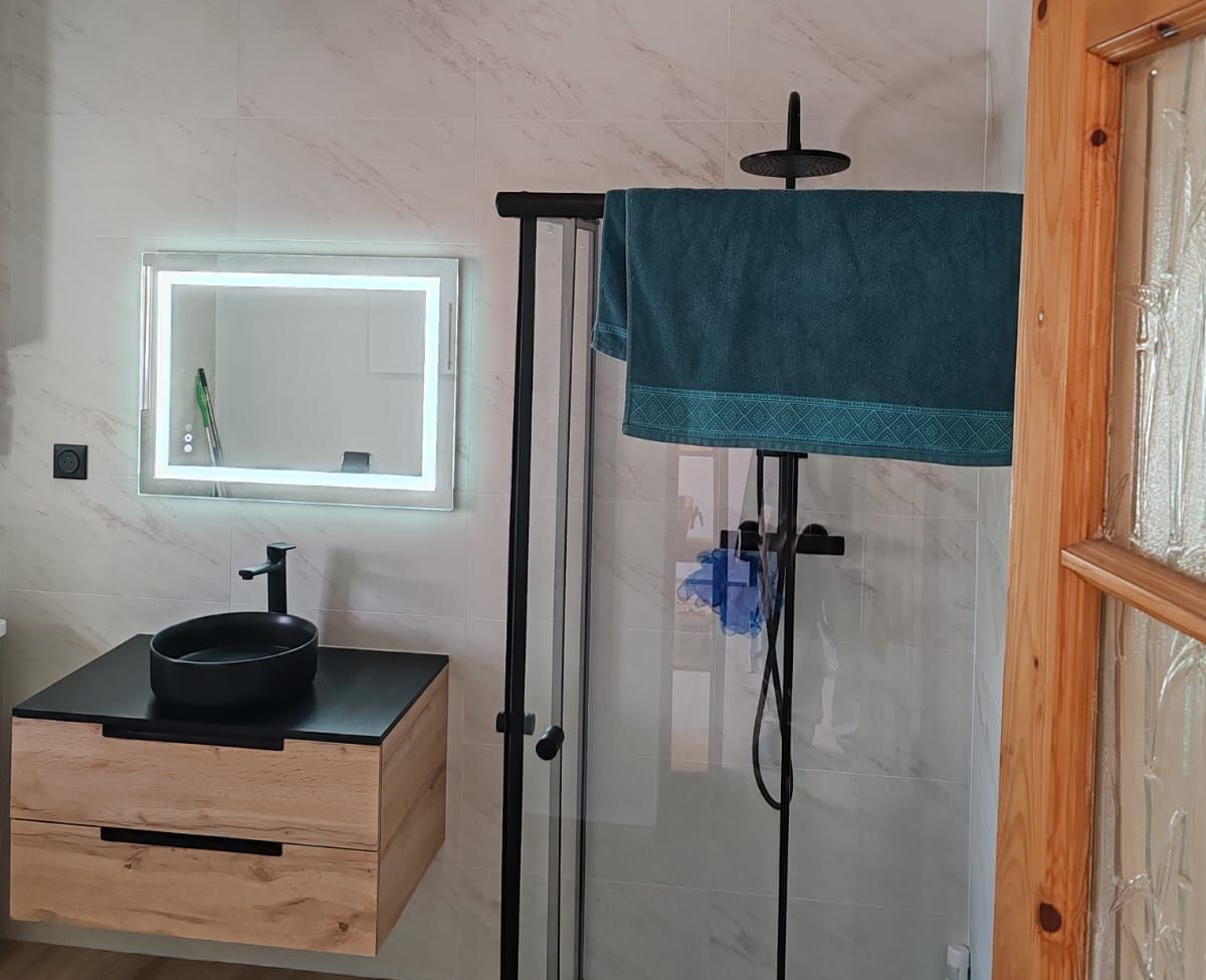Petite salle de bains avec lavabo, miroir et espace douche recouvert d'une serviette bleue.