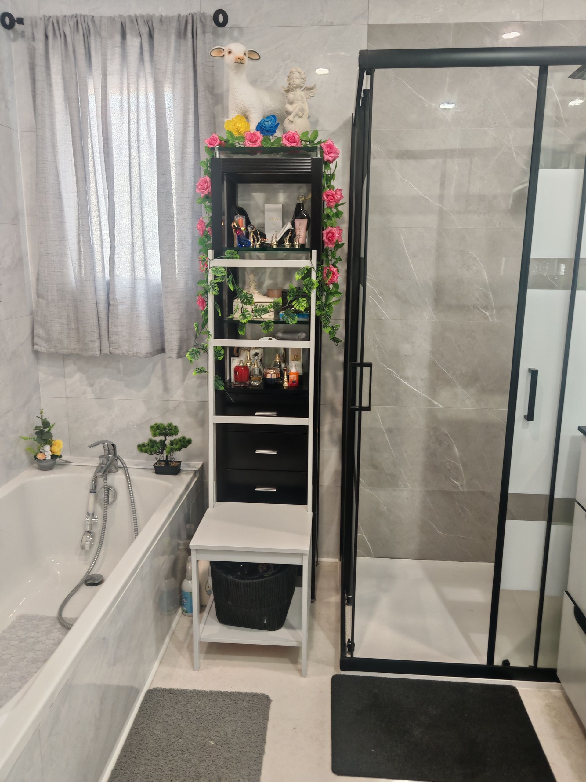 Salle de bains avec baignoire, cabine de douche, étagères et tapis gris près d'une fenêtre.