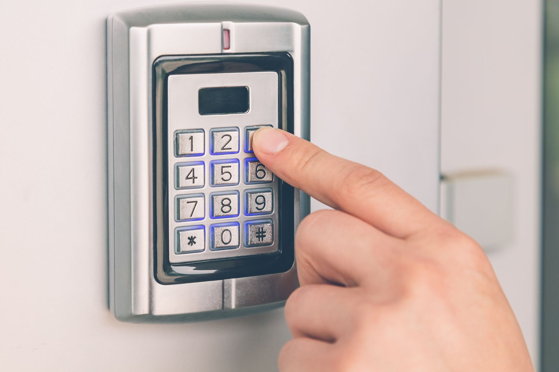 Une main appuie sur la touche 3 d'un clavier numérique argenté fixé à un mur blanc pour une entrée sécurisée.