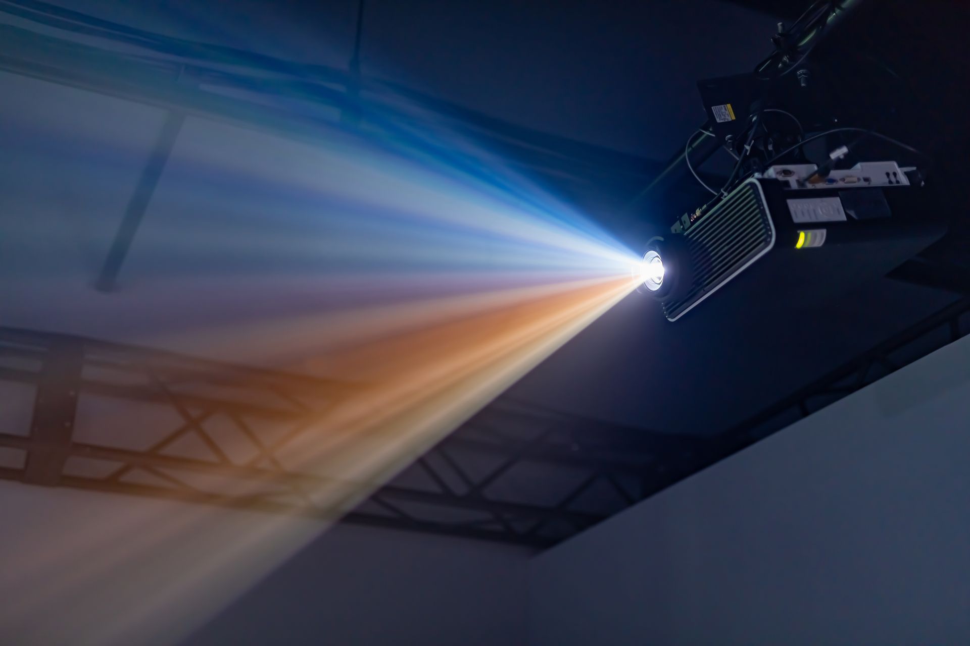 Un projecteur fixé au plafond projette un faisceau lumineux passant du bleu à l'orange dans une pièce sombre.