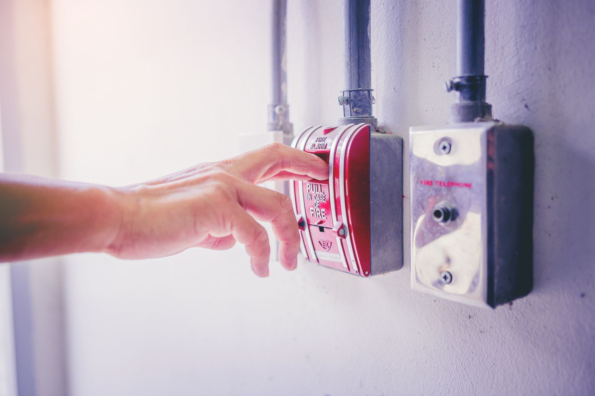 Une main se tend pour toucher un déclencheur d'alarme incendie rouge fixé au mur.