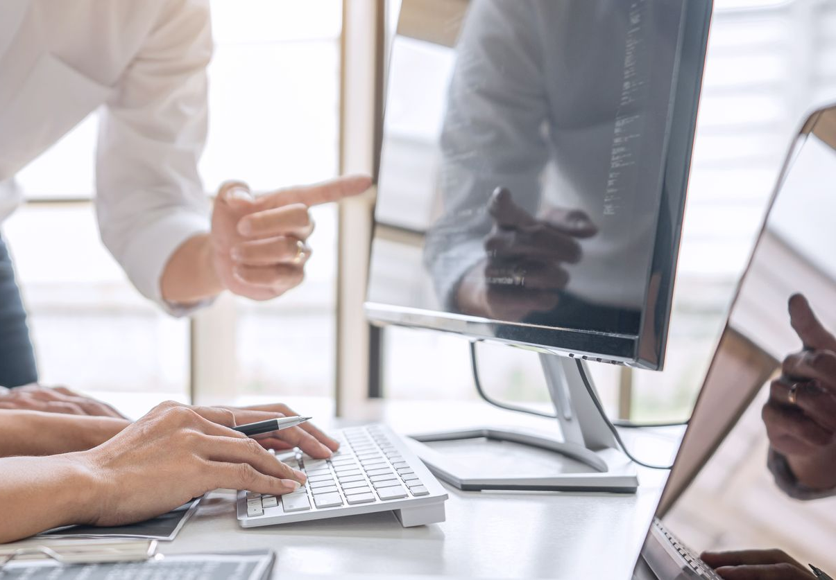 Des mains pointent vers un écran d'ordinateur lors d'une réunion professionnelle.