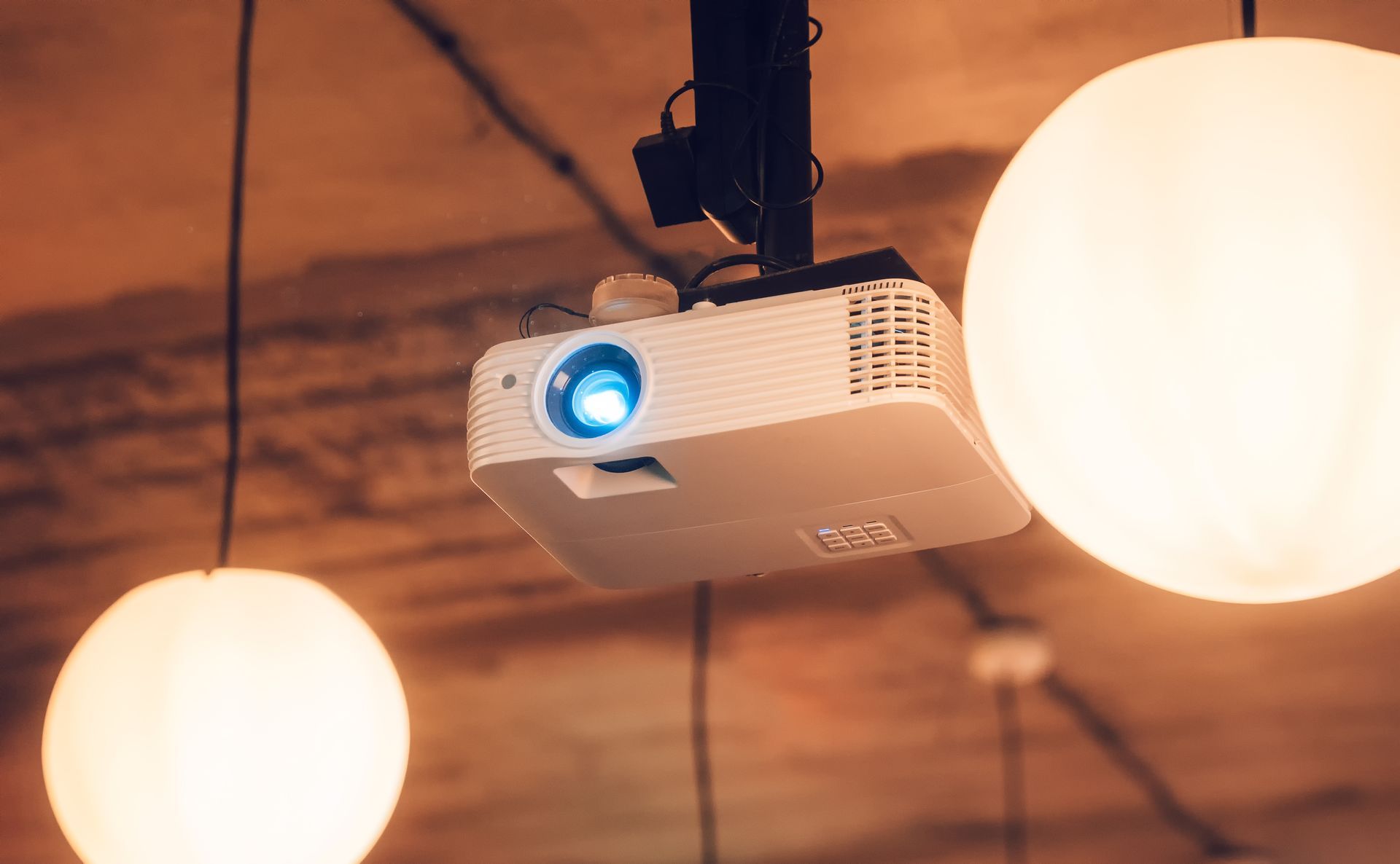 Un projecteur numérique blanc est suspendu au plafond entre deux suspensions lumineuses rondes.