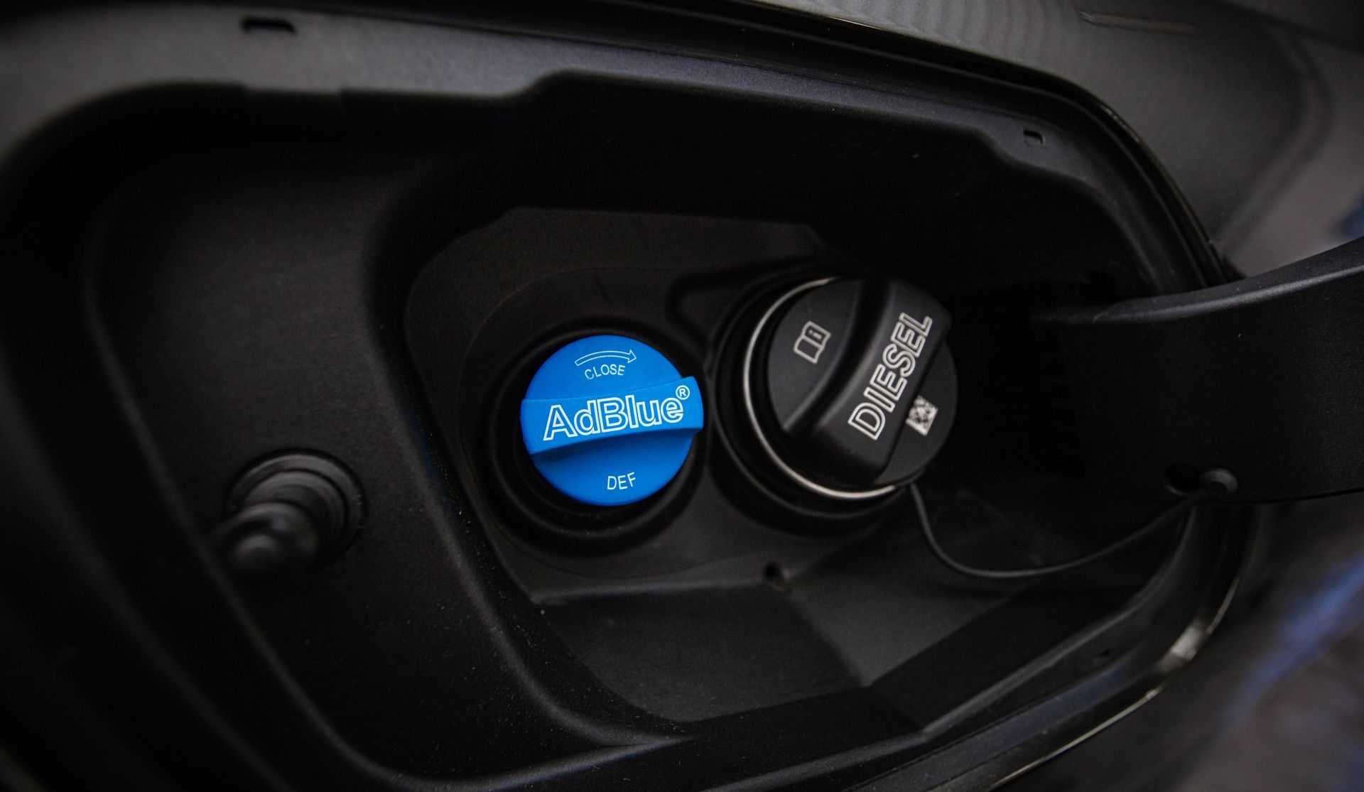 Une trappe à carburant de véhicule contenant un bouchon de remplissage de diesel noir à côté d'un bouchon plus petit, bleu, pour la solution d'urée AdBlue.