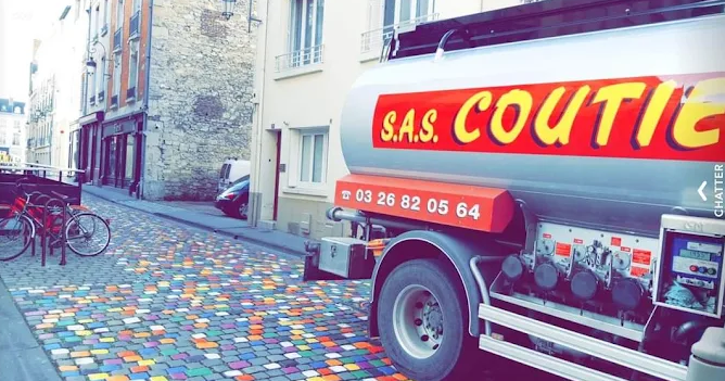 Un camion-citerne portant l'inscription « SAS COUTIEZ » est stationné dans une rue pavée de pavés multicolores façon mosaïque.