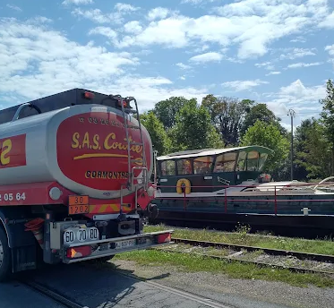 Un camion-citerne argenté et rouge garé à côté d'une péniche verte et blanche par une journée ensoleillée.