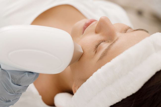 Femme recevant un soin du visage avec un appareil portatif blanc et un bandeau en forme de serviette