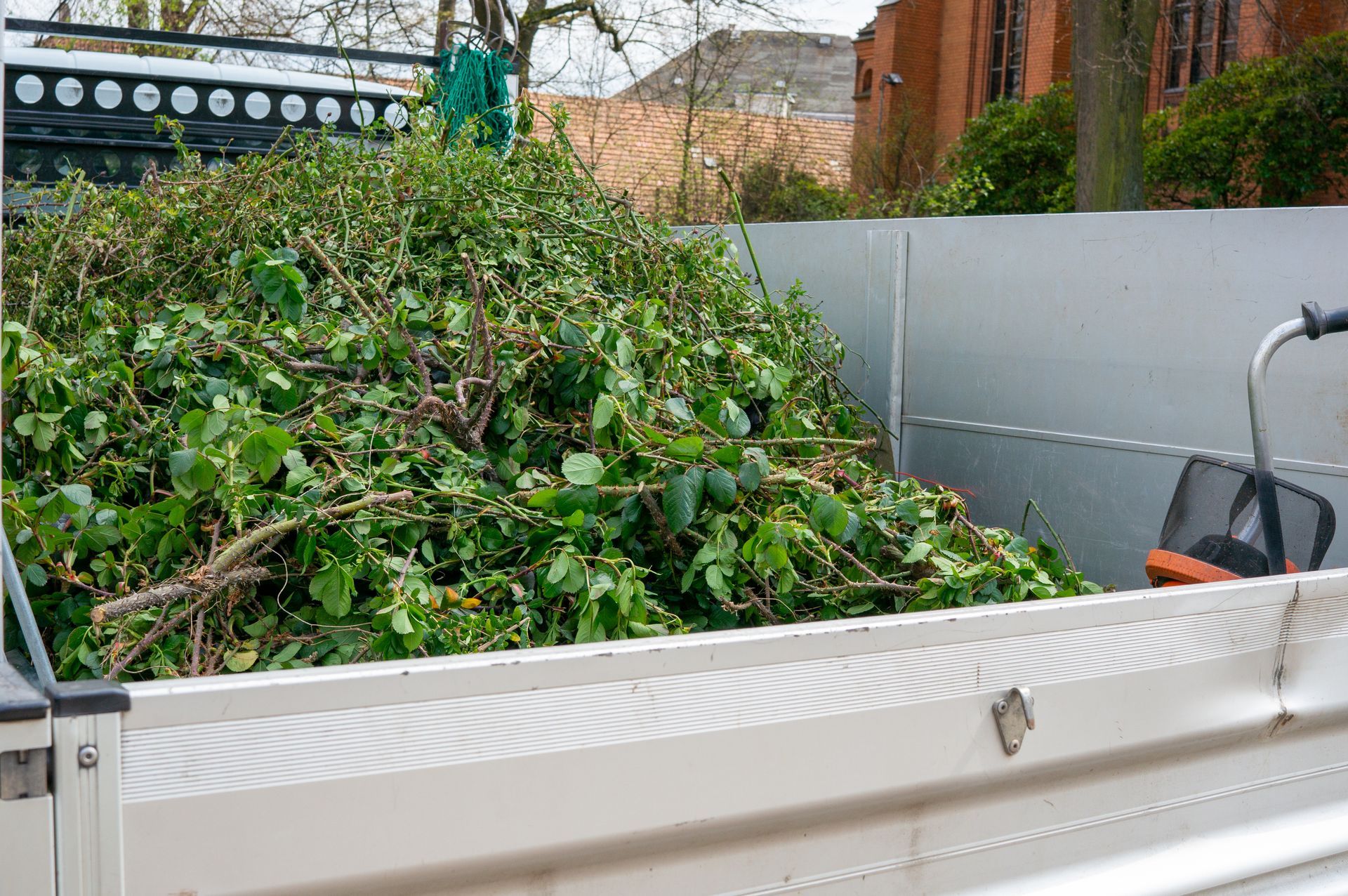 Remorque utilitaire blanche remplie de déchets verts et de branches, à l’extérieur.