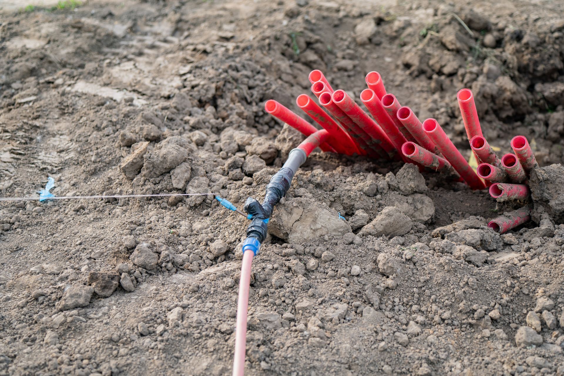 Des tubes rouges en forme de tuyaux qui dépassent d’un monticule de terre, à côté d’un câble rose.