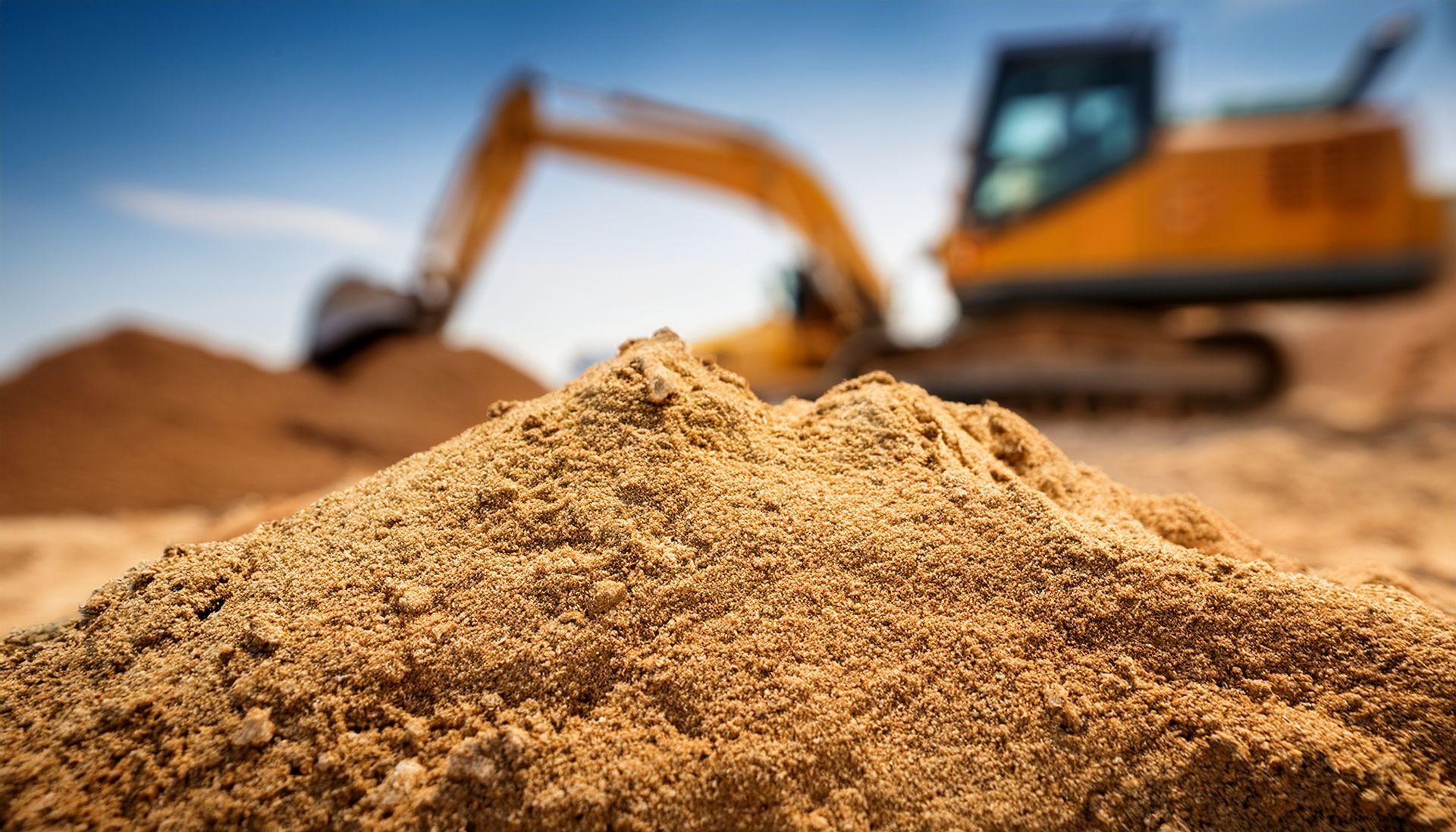 Une excavatrice creuse le sable sur un chantier, avec un monticule de sable au premier plan.